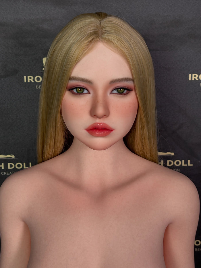 A doll with long blonde hair, green eyes, and pink lips, shown from the shoulders up against a dark branded backdrop.