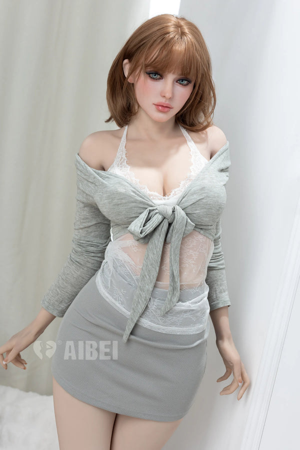 A doll with short auburn hair wearing a light gray off-the-shoulder long-sleeve top with a large front bow, sheer mesh panels, and a matching gray mini skirt, posed against a white curtain background.