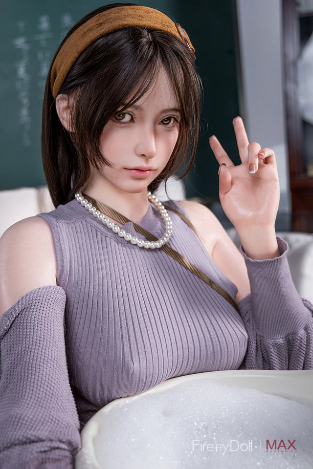 A close-up portrait of a doll wearing a ribbed lavender sleeveless top, a brown headband, and a pearl necklace, making a peace sign. The background is a softly blurred indoor setting with a chalkboard.