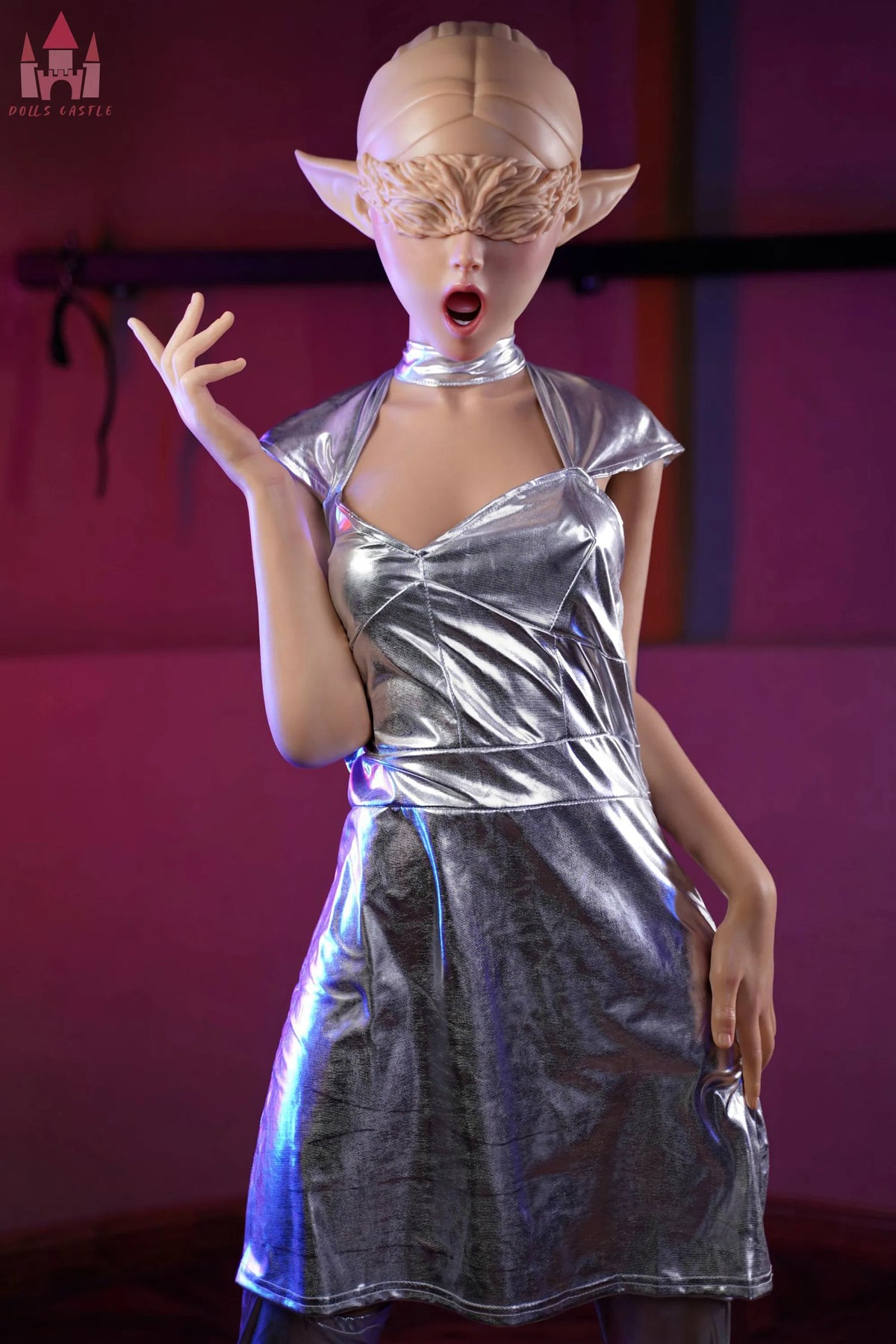 A collectible action figure of a female elf character wearing a shiny metallic silver halter dress and matching blindfold mask, posed against a dark pink background.