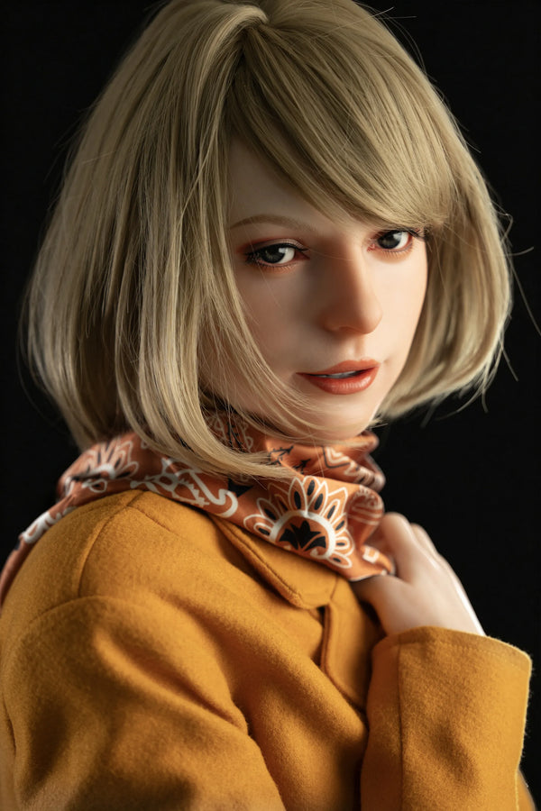 A close-up portrait of a doll with short blonde hair, wearing a mustard yellow coat and a patterned scarf, set against a solid black background.